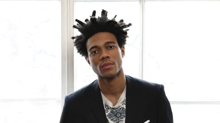 Man standing facing the camera with his hands in his pockets. There is a window in the background.