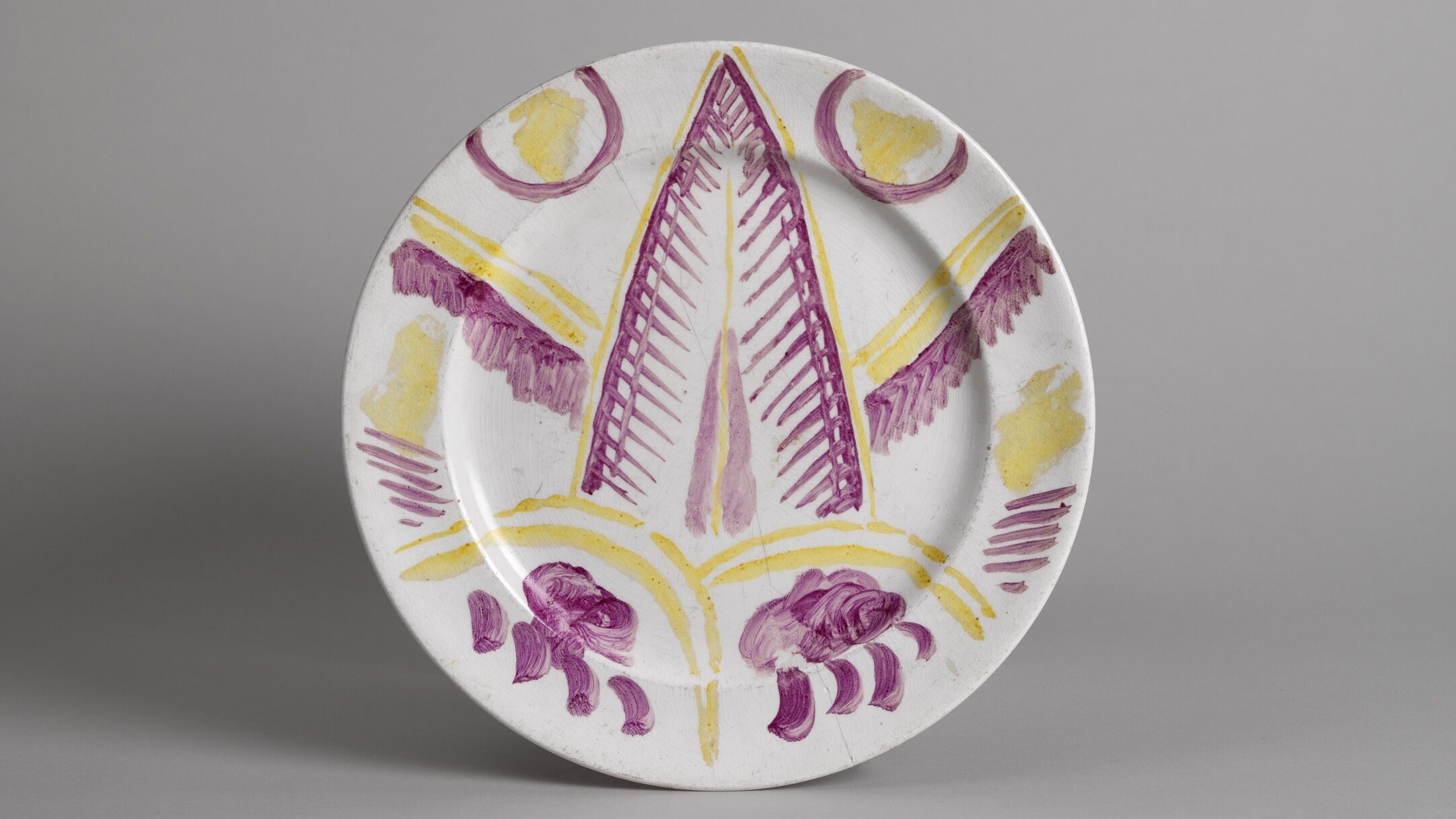 Plate with overglaze painted design of a cat’s face and paws, decorated in yellow and purple paint