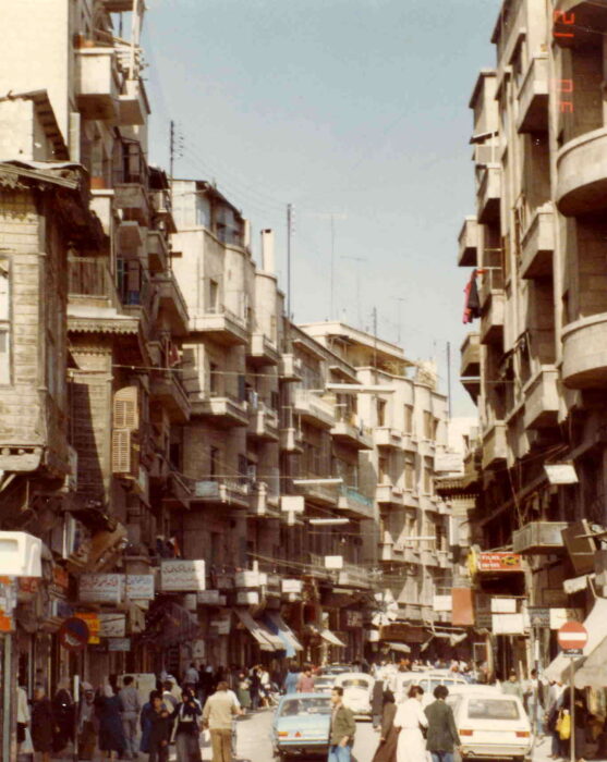 A street of tall narrow houses; below cars and people bustle.