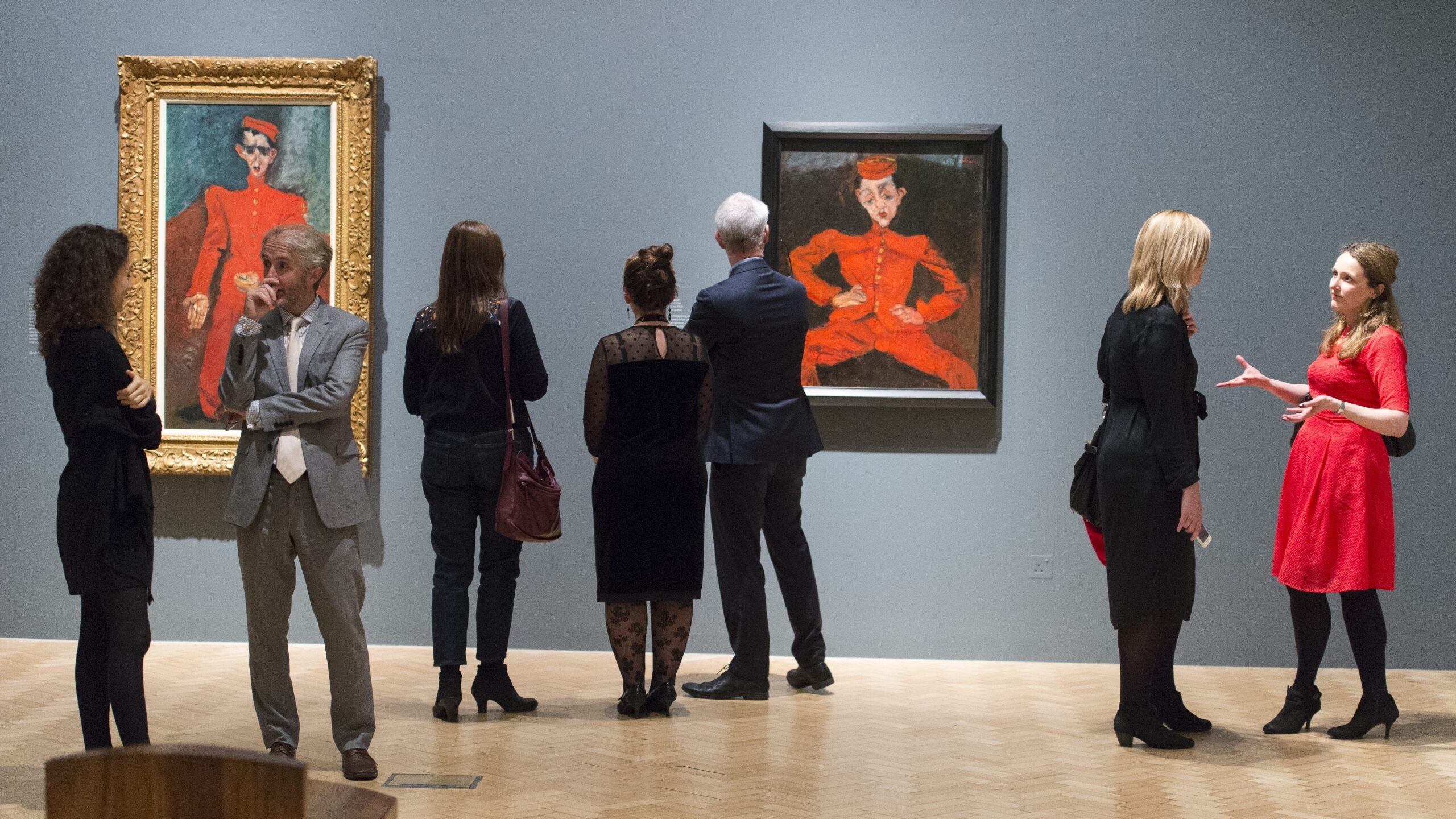 A group of people standing in a gallery looking at paintings hanging on the wall