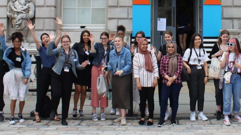 Cohort from 2019's Summer University posing for a photo, some with their hands in the air, outside The Courtauld Gallery at Somerset House