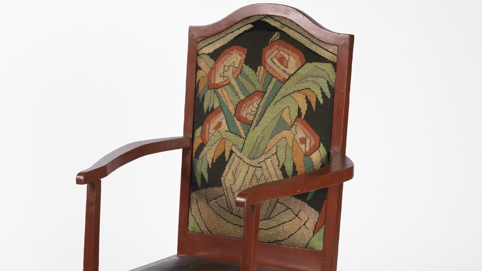 A chair with an embroidered floral seat back and a black seat cushion