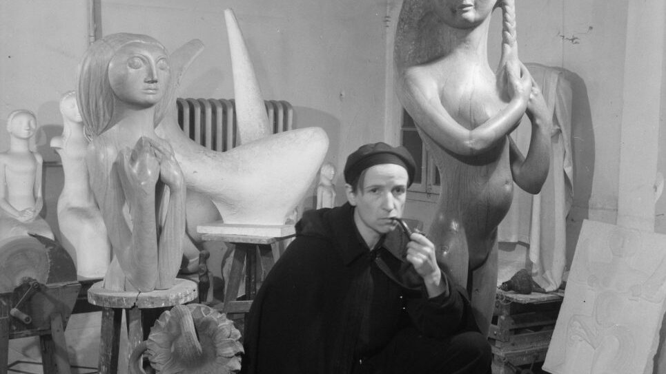 photograph of artist sat in room with sculptures