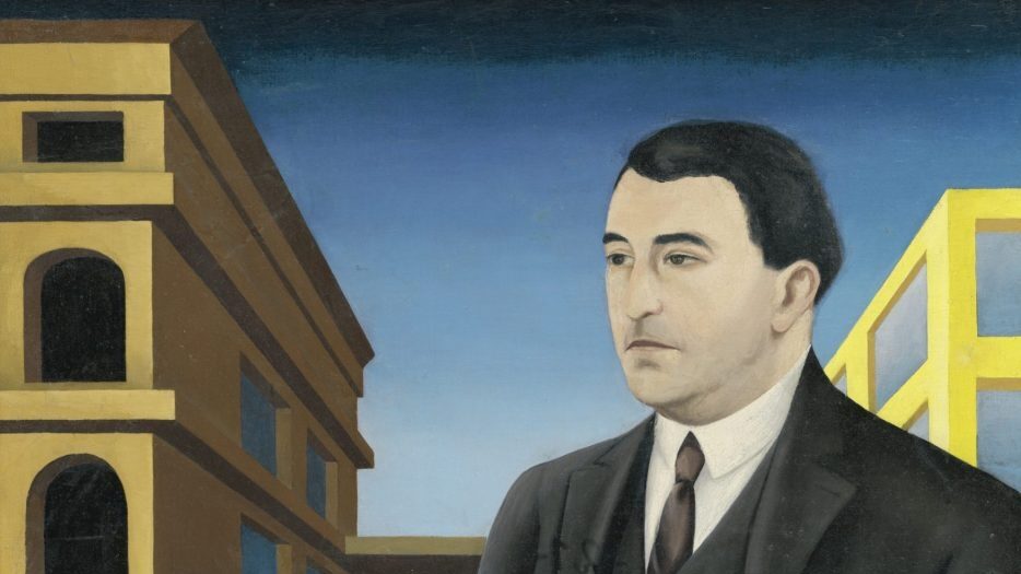 man in a suit is stood infront of a yellow building. between them is a table with an orange tablecloth and a metal ornament jug of some kind.