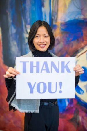 A woman holding a piece of paper with 'thank you' on it.