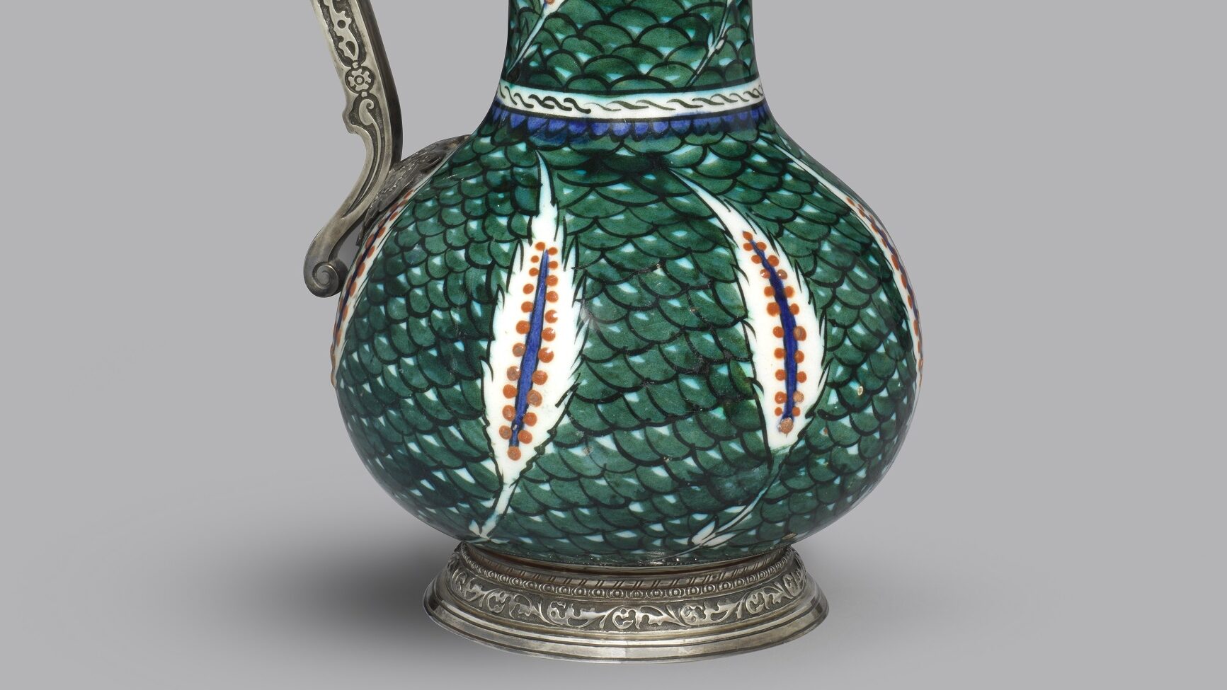 Ornate jug with saz leaves on a green fish-scale ground and an embellished curved silver handle and rim, Circa 1560