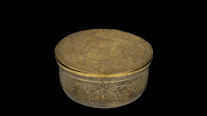A golden, rounded bowl with a flat lid. Highly detailed engraving covers the entire bowl in traditional Islamic patterns.