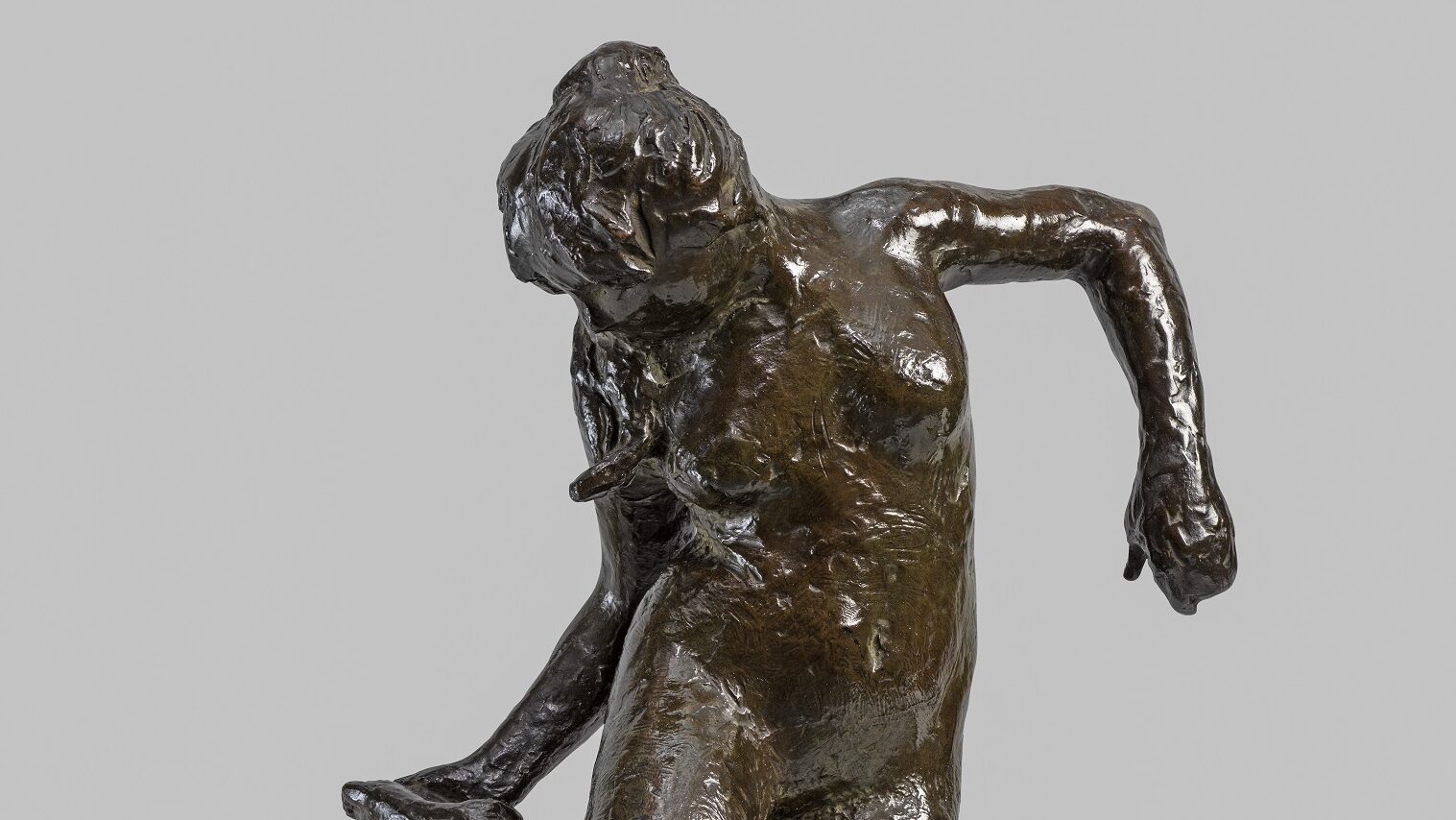 A bronze sculpture of a dancer looking at the sole of her right foot