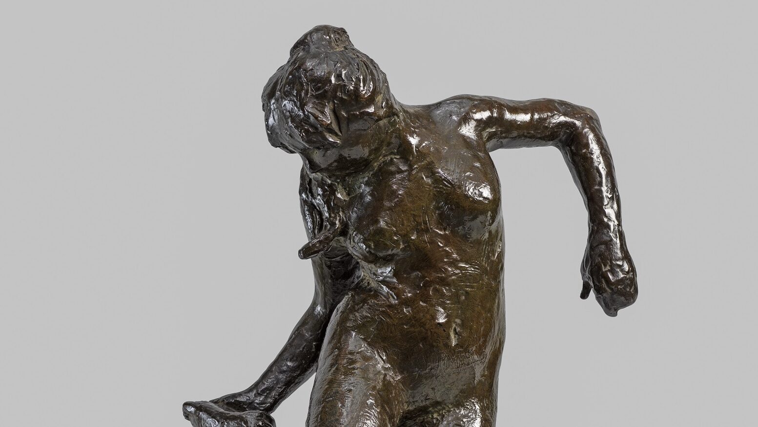 A bronze sculpture of a dancer looking at the sole of her right foot