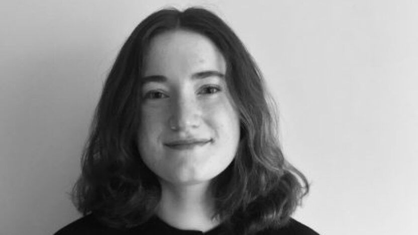 Black and white headshot of Zaena Sheehen, smiling, against a black backdrop.