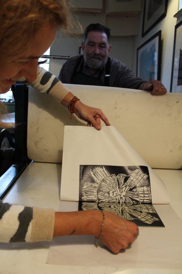 a lino print being revealed from a roller print press