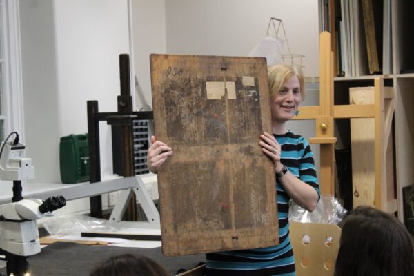 a lady holding up a painting to show its back and the author marks