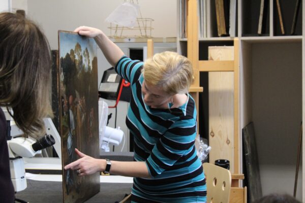 a lady pointing at an area of a painting being conserved