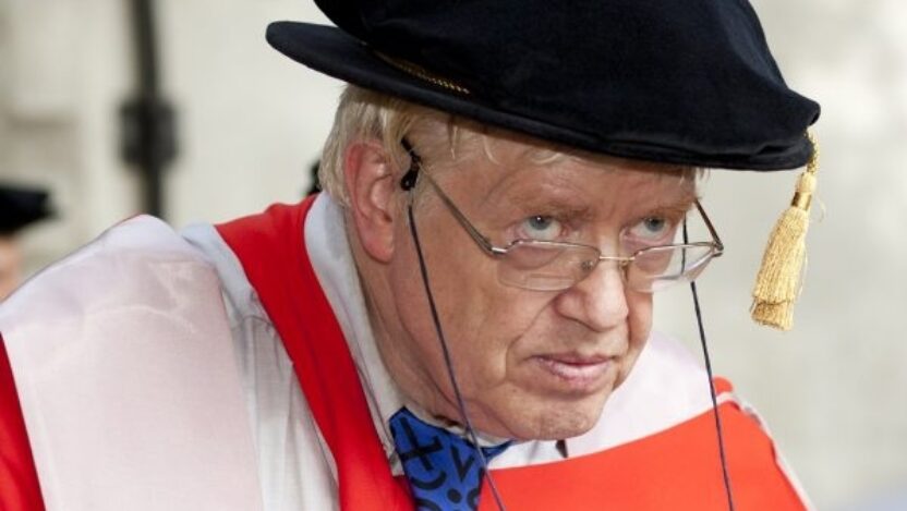 Professor Robert Suckale wearing a graduation cap, glasses, blue and black patterned tie, shirt, and red graduation gown. Taken at The Courtauld Graduation Ceremony, 2011.