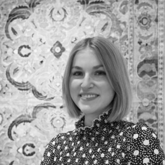 A woman with short blond hair smiling in front of a Safavid carpet