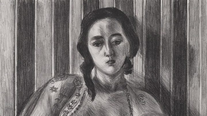 A nude woman sits on the floor, left leg drawn to her chest and right leg outstretched, with a vacant gaze. She is wearing a sheer, embroidered, open blouse. The wall behind her has a dark and light vertical stripes, and on the floor she sits on a flowery embroidered rug. A signature indicates the print is 33/50.