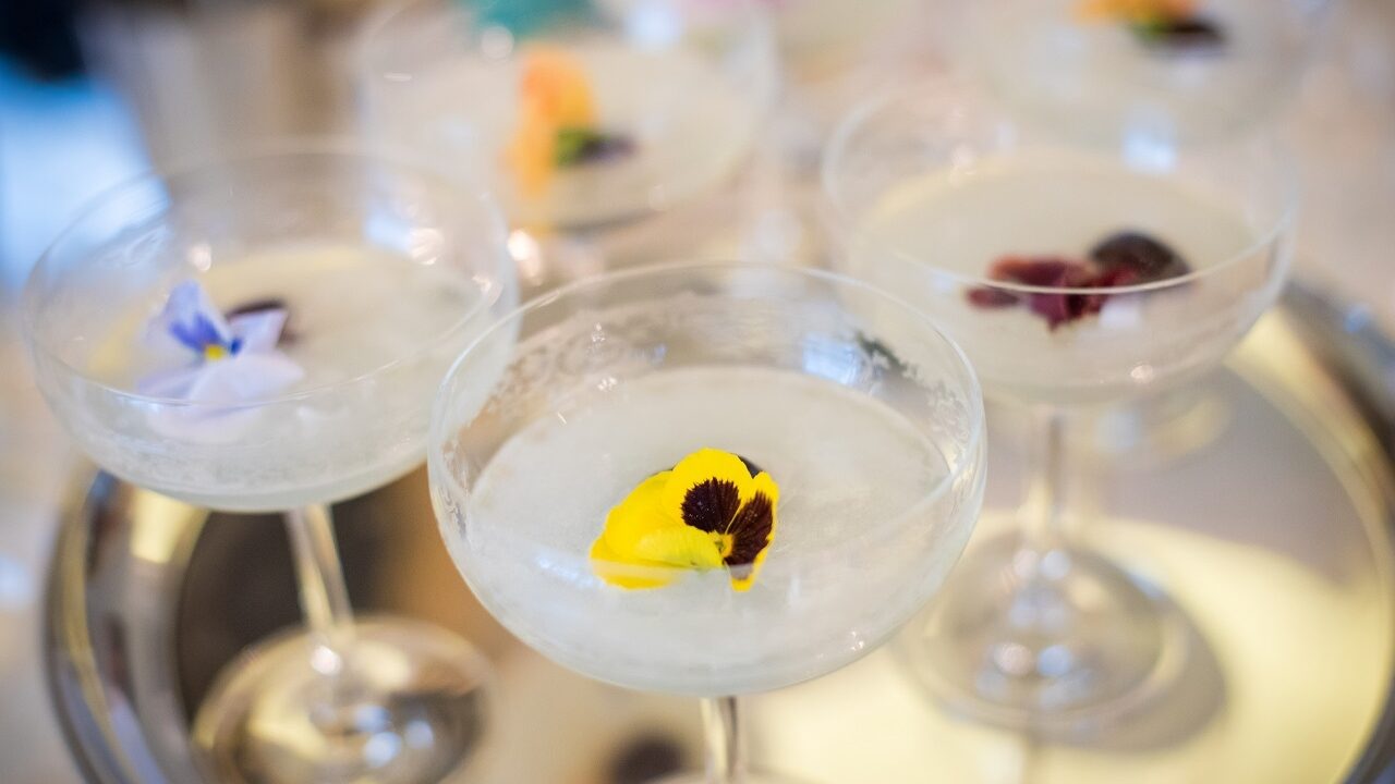 Cocktails with colourful edible flowers presented on a silver tray