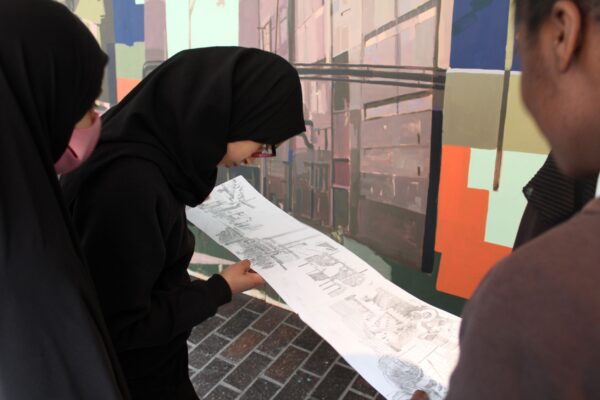 Y9 students look closely at a preliminary sketch in front of the large scale mural