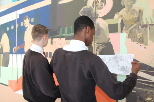 Y9 students look closely at a preliminary sketch in front of the large scale mural