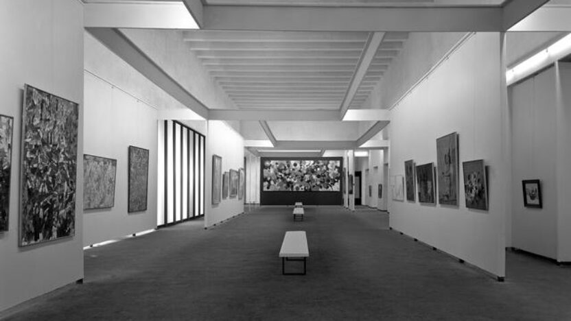 Photograph showing abstract artworks by Jackson Pollock in black and white hung in a white box gallery with benches throughout the room