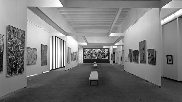 Photograph showing abstract artworks by Jackson Pollock in black and white hung in a white box gallery with benches throughout the room