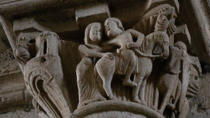 Photograph of a stone carving at the top of a pillar depicting a man on a horse turning backwards to embrace a woman