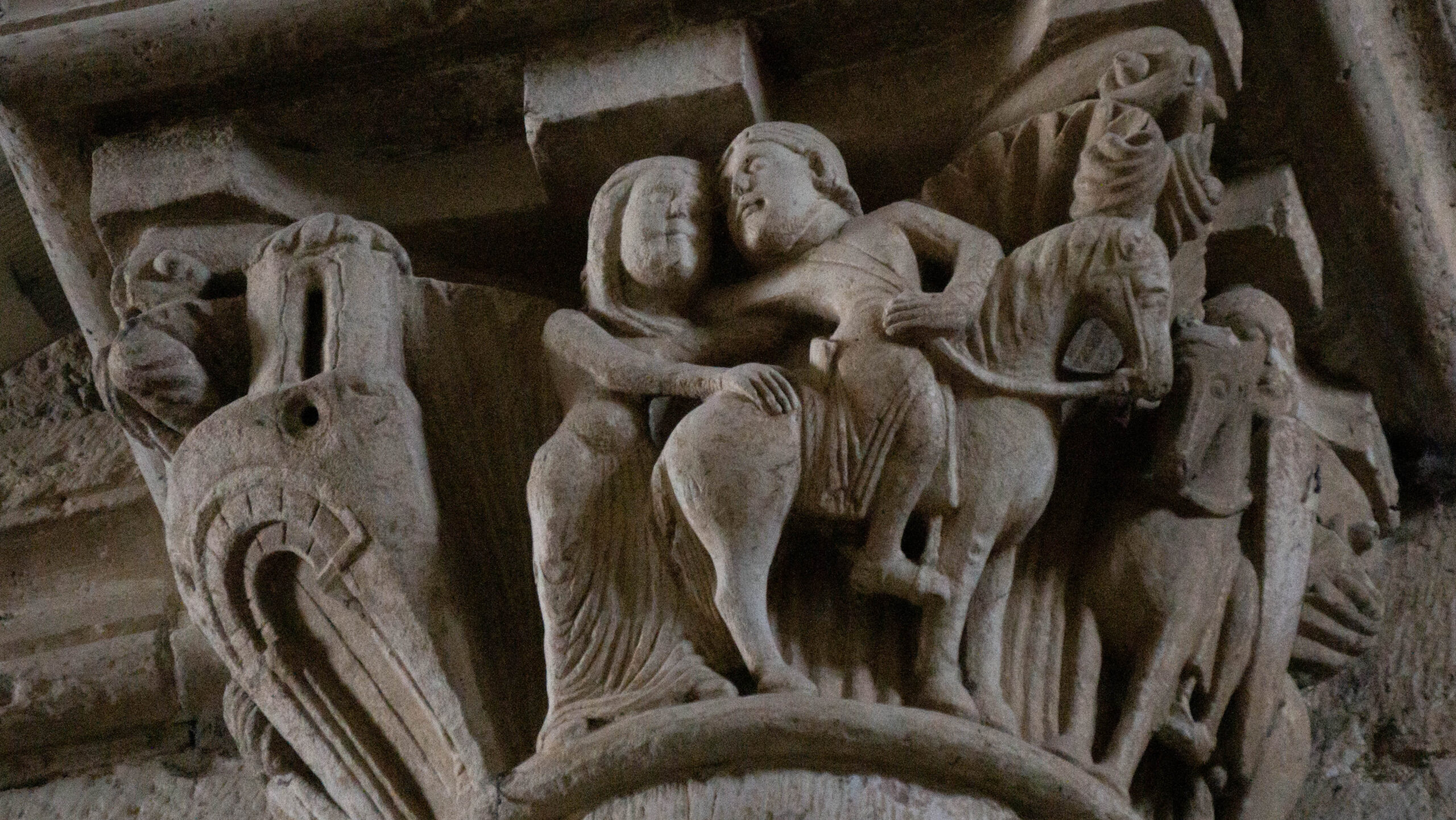 Photograph of a stone carving at the top of a pillar depicting a man on a horse turning backwards to embrace a woman