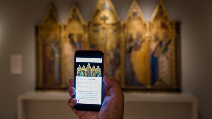 An image of a visitor holding up their phone with the Bloomberg Connects guide showing, in the gallery