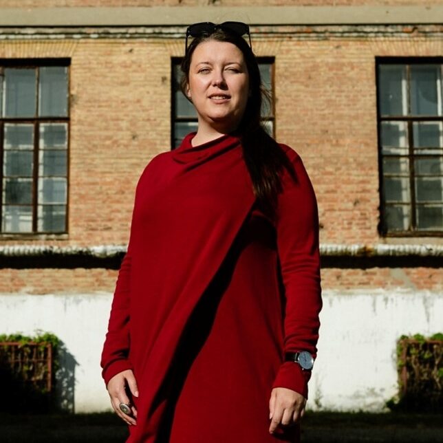portrait of a woman wearing a red overall standing in front of a building