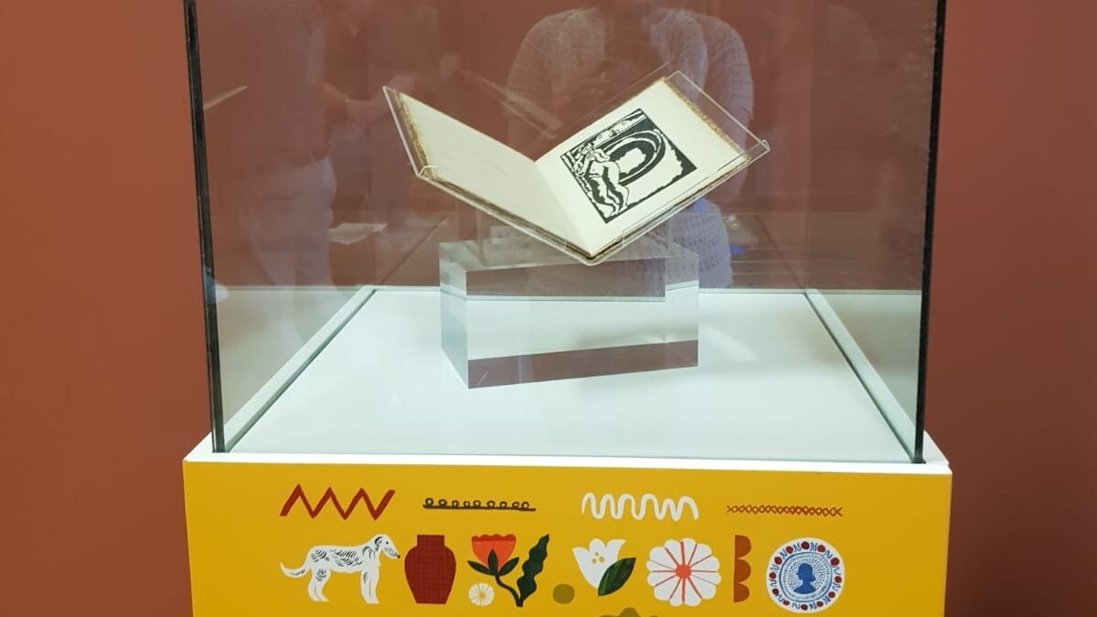 Photograph showing a book in a glass case standing on a brightly coloured plinth