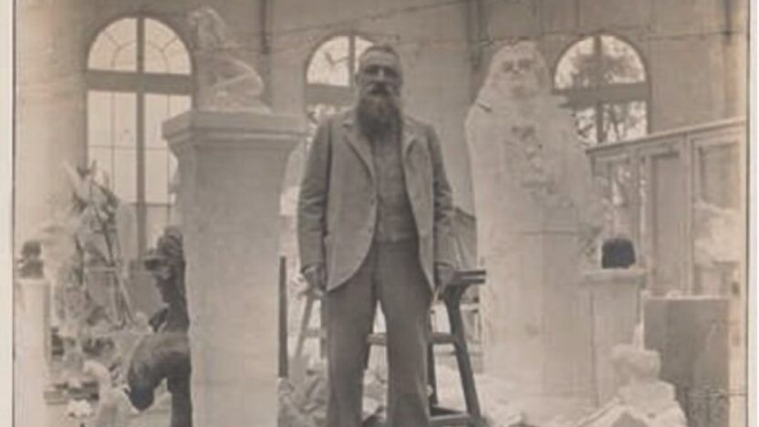 Black and white photograph of the artist Rodin standing on a platform in his studio surrounded by parts of sculptures