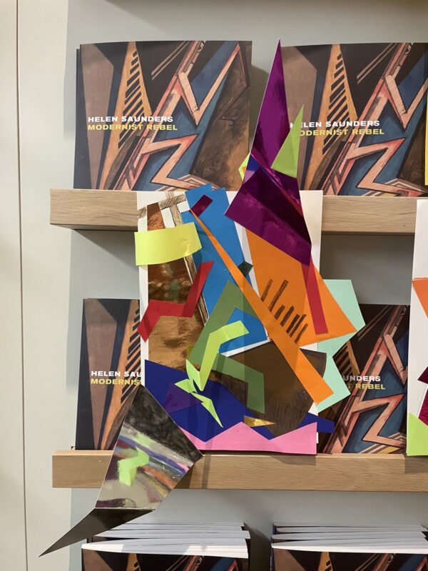 two colorful abstract drawings on a shelf with books in the background