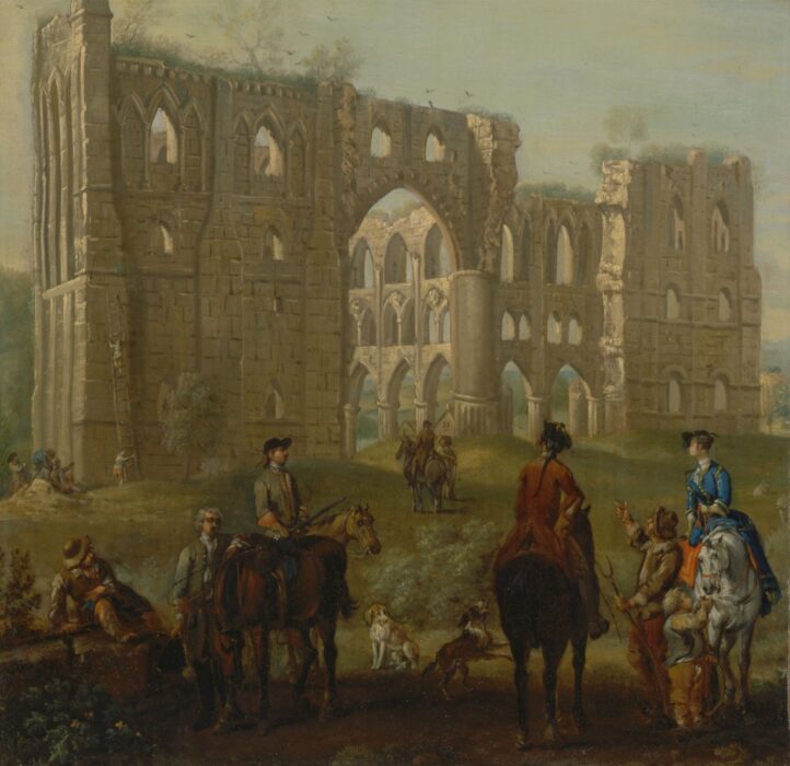 A group of people, some on horses, stand in front of the ruins of Rievaulx Abbey.
