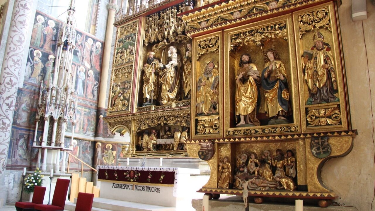 Photograph of a richly decorated alterpiece with three chairs in front of it