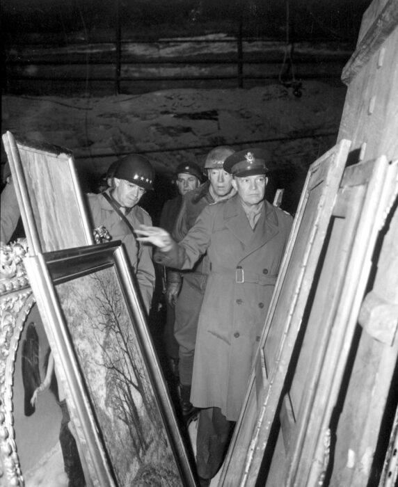 Four men look through paintings stacked in a cave.