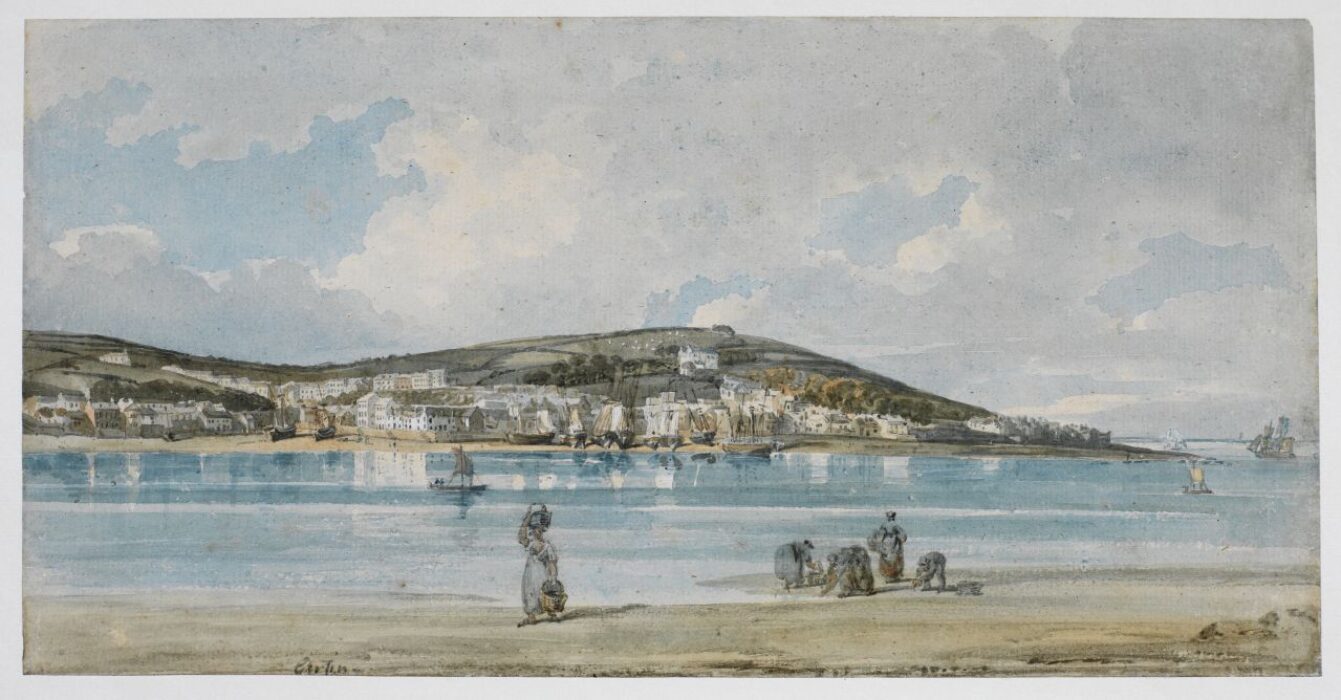 Five people stand on a beach. On the other side of the water, in the distance, is a small town.
