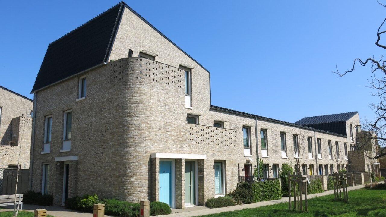 Photograph of a grey building against a blue sky. There are bollards to the left of the building and grass and trees in front of it.
