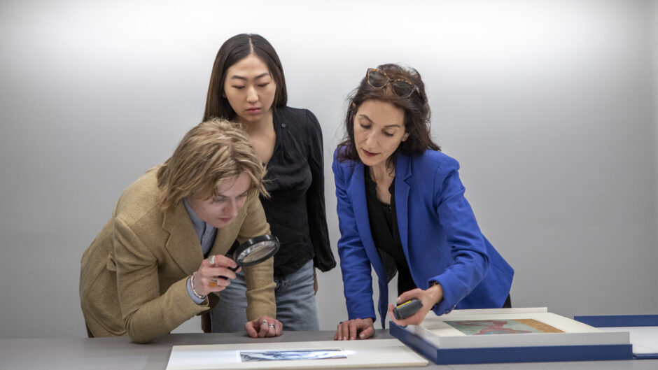 group of three students observing a print with a migmifying glass
