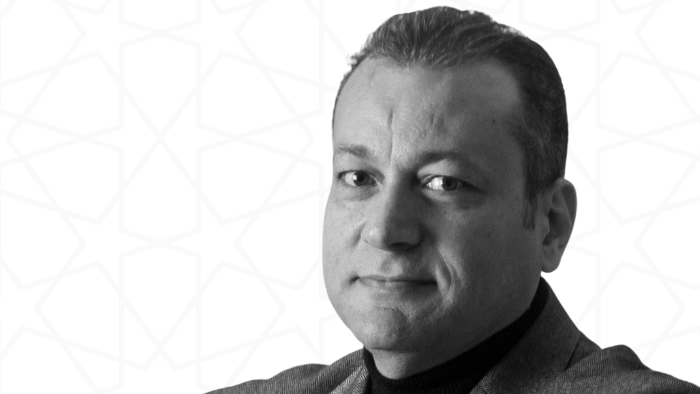 Black and white photograph of a man wearing a blazer, facing the camera and with his arms crossed