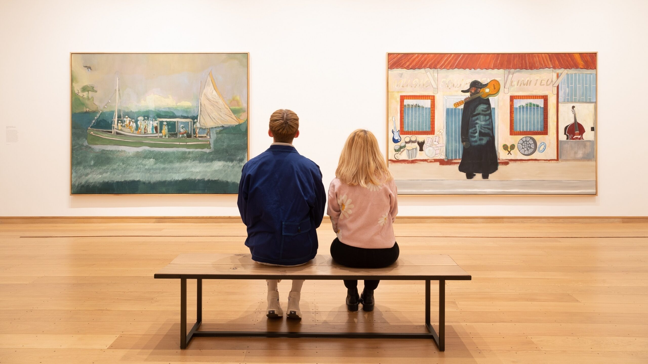two young people sitting on a gallery bench observing Peter Doig's paintings