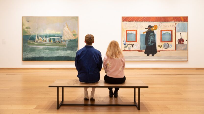 two young people sitting on a gallery bench observing Peter Doig's paintings