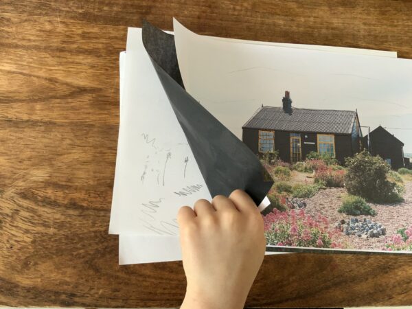 image of a hand pulling up a carbon copying sheet to reveal the drawing underneath