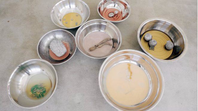 Photograph showing 7 silver metal bowls of different sizes with different objects inside, set on a stone surface