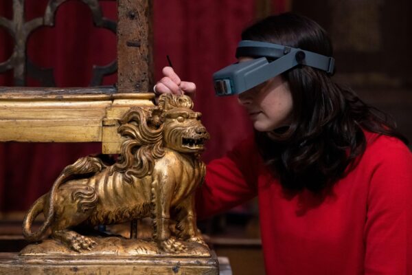 Krista, wearing a conservation magnifying headgear as she does conservation work on a gilded lion, part of the Conservation Chair.