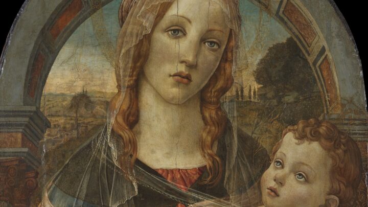 Oil painting of a Virgin and Child, with the Virgin standing in front of an archway wearing an orange-red dress and blue cape holding an infant lightly swaddled. The colours are vibrant but the panel visibly worn.