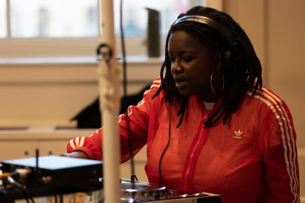A DJ with a red tracksuit top, headphones and black hair at The Courtauld Lates