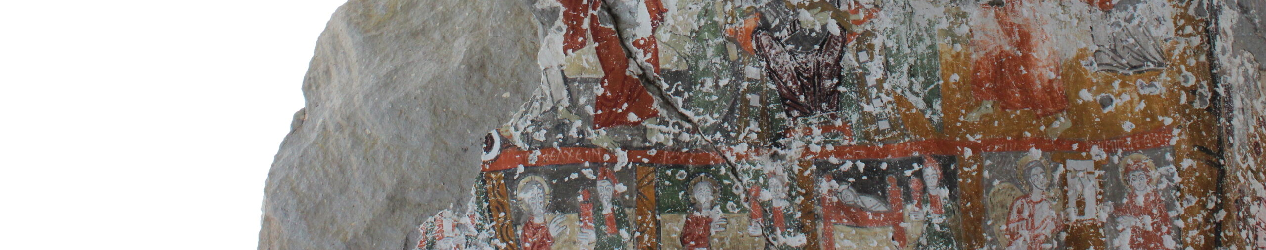 Image of an incomplete wall depicting a cross. The wall is missing a section at the top and sections of rock are visible in the background through this gap.