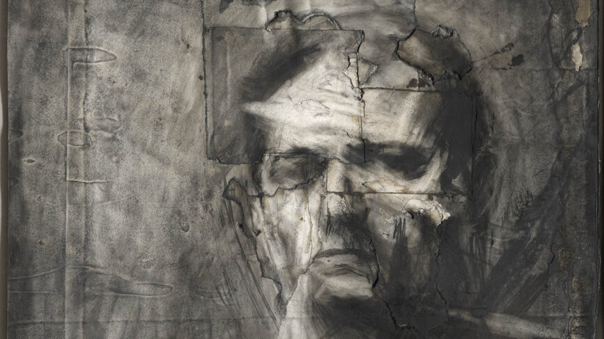 Charcoal drawing of a man, Frank Auerbach, sitting slightly side-on to the viewer and staring at us with a stern expression. The background is roughly completed, and the face somewhat fragmented by the background.