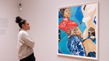 A woman looks at an artwork of a woman a red top against a blue background