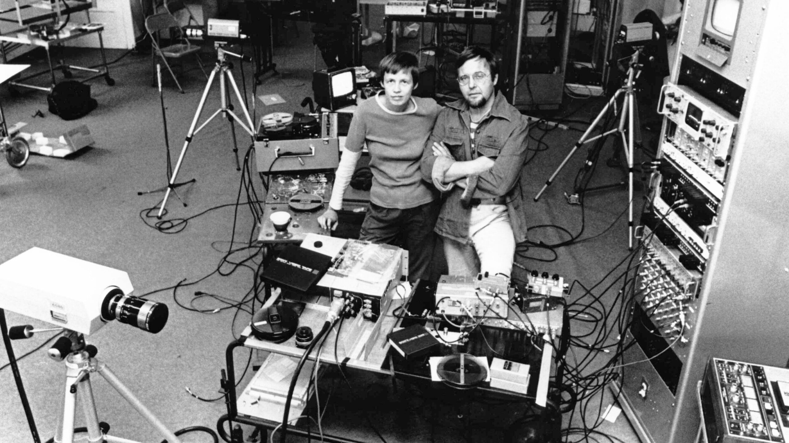 Black and white photograph of two people in a studio surrounded by cameras and filming equipment